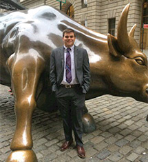 a Student in a business suit take a picture in front of the Wall St. Bull