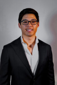 Asian male with glasses wearing black blazer and light grey shirt.